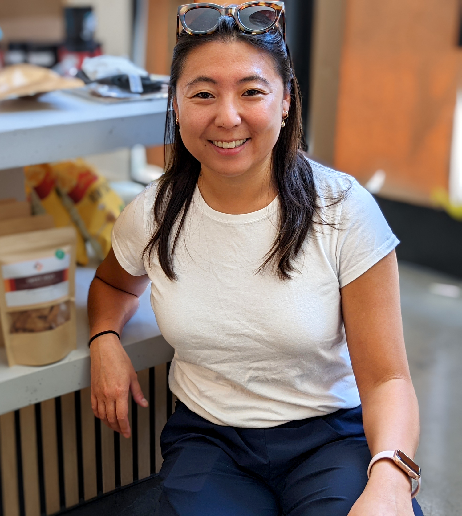 Asian American Founder of Wei Good Food, ZiWei Li, kneels while leaning on a shelf containing Wei Good Food products